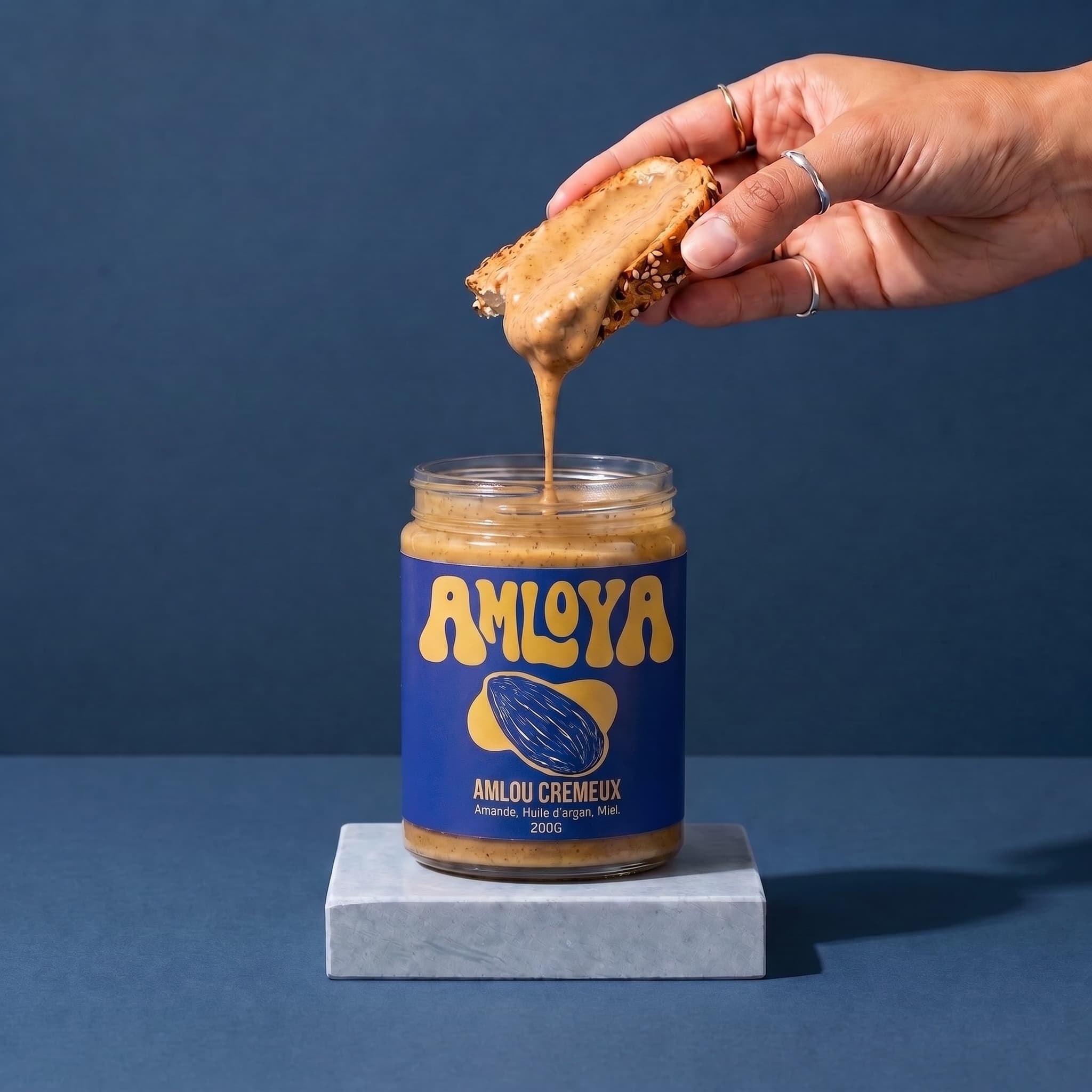 L'amlou crémeux qui coule d'une tartine au-dessus du pot AMLOYA ouvert