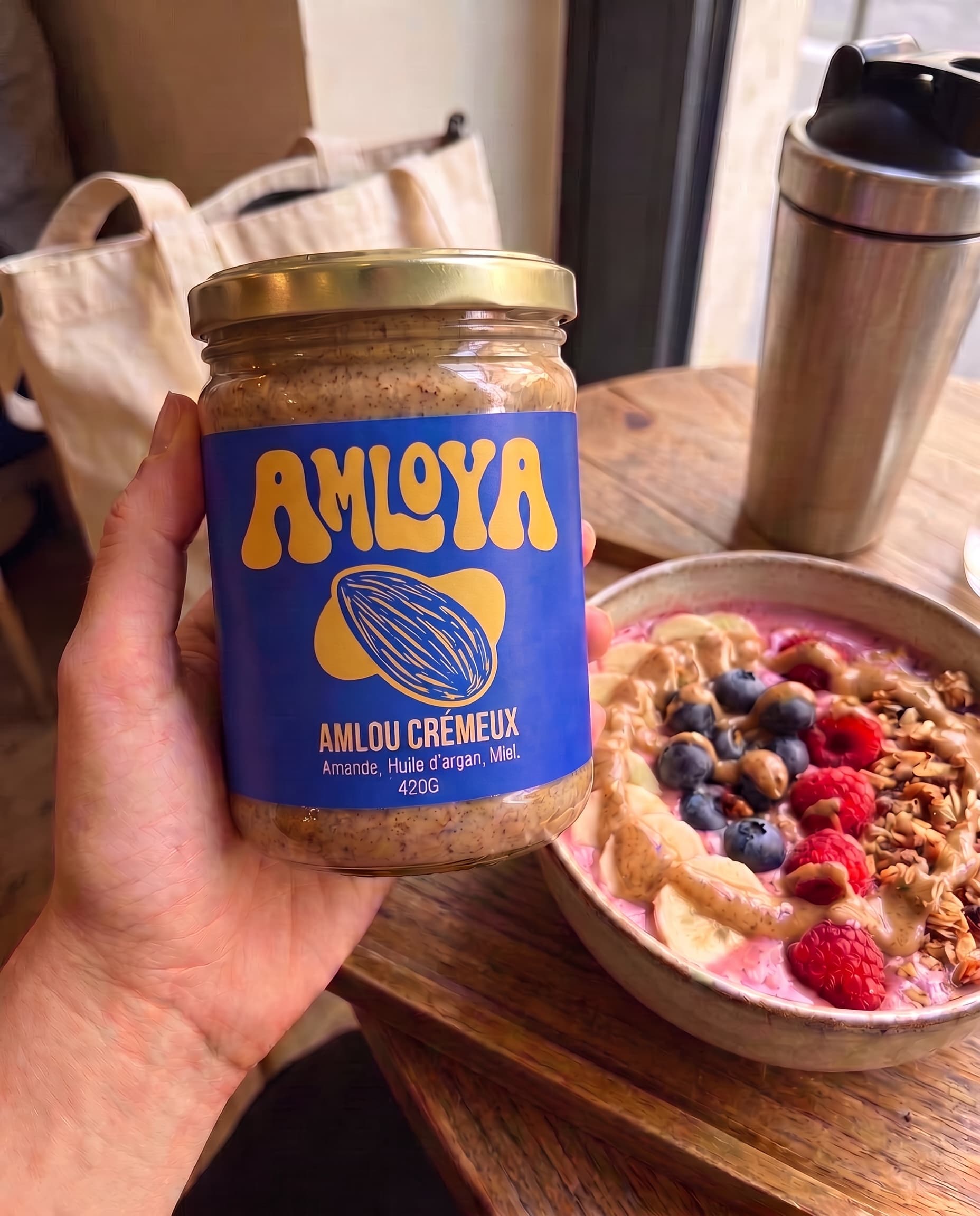 Main tenant le pot AMLOYA au-dessus d'un smoothie bowl à l'amlou